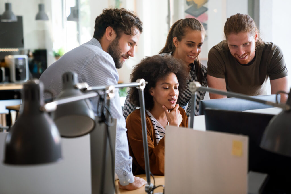 Diverse group of professionals meeting in office. IT programmers use computer, talk strategy